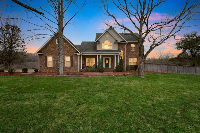 traditional-style house featuring fence, a lawn, and brick siding