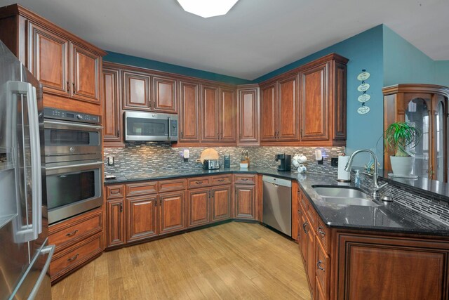 kitchen with stainless steel appliances, tasteful backsplash, a sink, and light wood-style floors