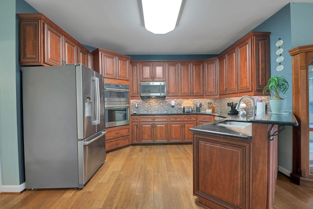 kitchen with light wood-style flooring, appliances with stainless steel finishes, a peninsula, a sink, and backsplash