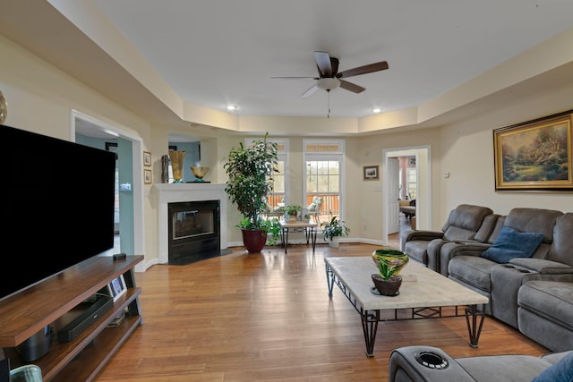 living area with a ceiling fan, a fireplace with flush hearth, baseboards, and wood finished floors