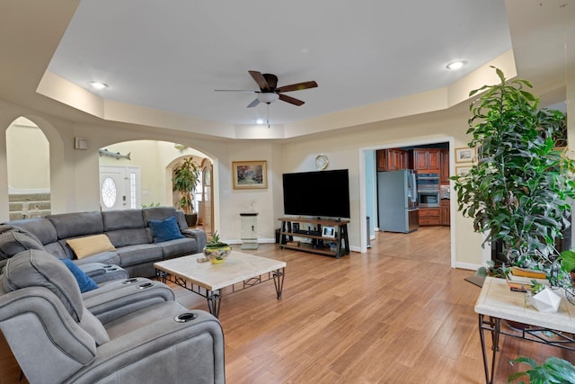 living room featuring light wood-type flooring, ceiling fan, arched walkways, and baseboards