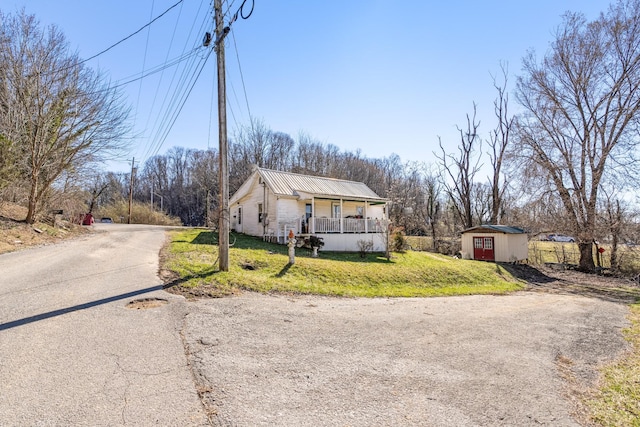 exterior space featuring metal roof, a porch, aphalt driveway, a shed, and a front yard