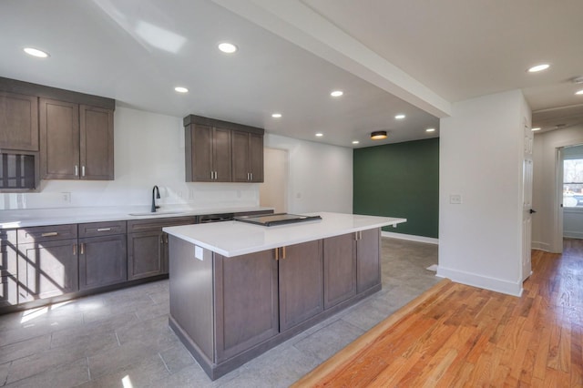 kitchen featuring a center island, recessed lighting, light countertops, a sink, and dark brown cabinets