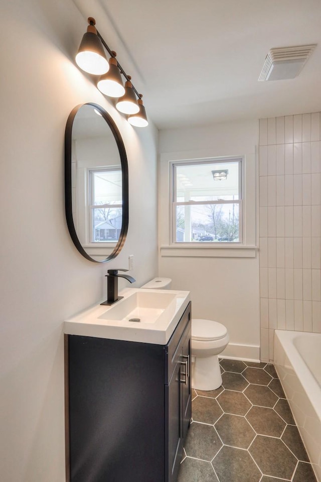 bathroom featuring toilet, visible vents, vanity, a bath, and tile patterned floors