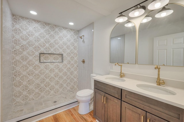 bathroom with wood finished floors, tiled shower, a sink, and toilet