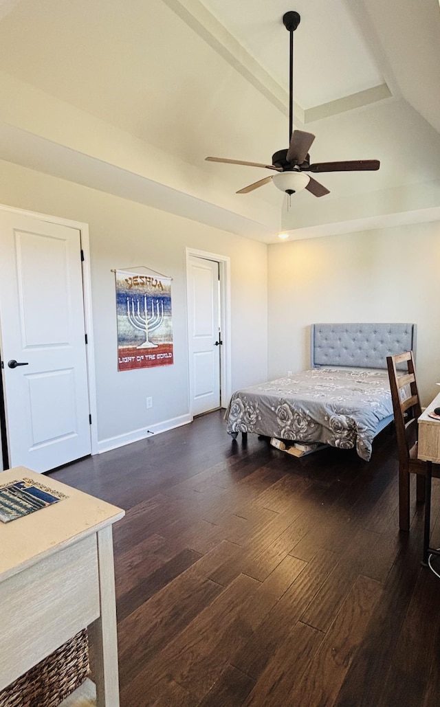 bedroom featuring a ceiling fan, a tray ceiling, dark wood finished floors, and baseboards