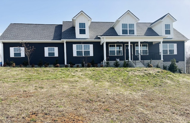 view of front of property featuring covered porch, a shingled roof, and a front lawn