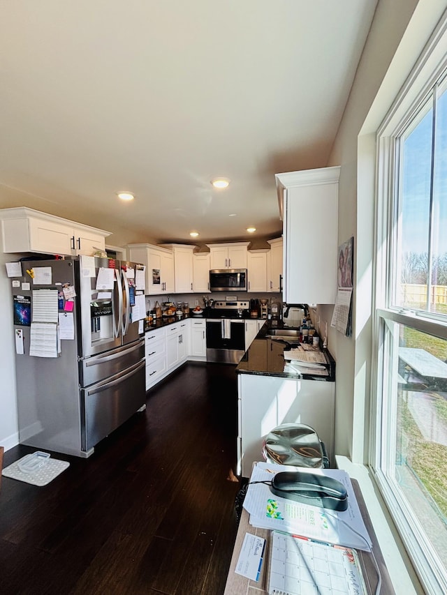 kitchen with dark wood-style flooring, a sink, white cabinetry, appliances with stainless steel finishes, and dark countertops