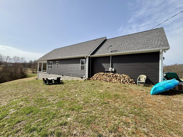 back of house with crawl space, roof with shingles, and a yard