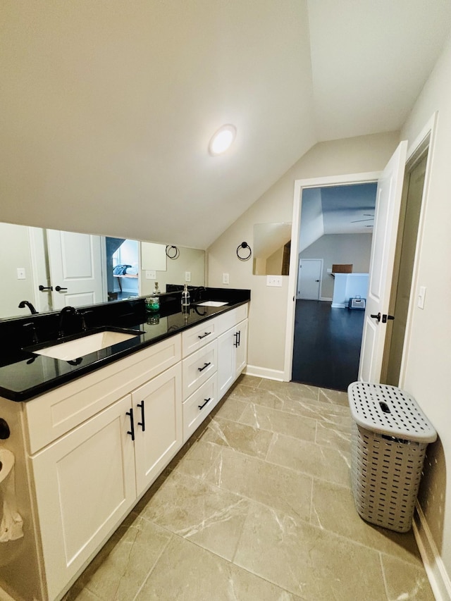 bathroom with vaulted ceiling, double vanity, a sink, and baseboards