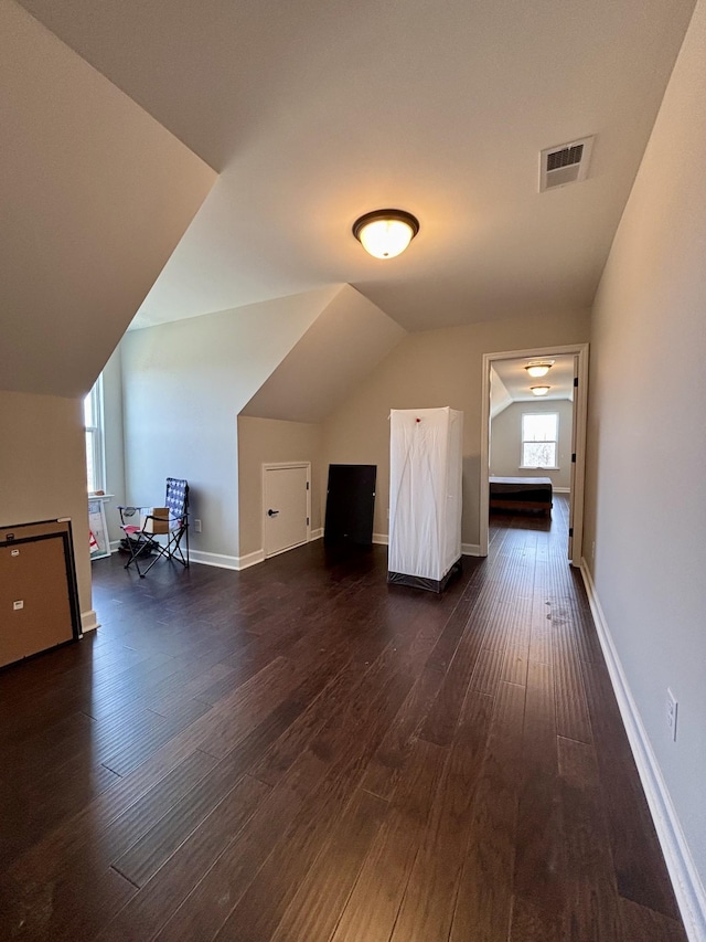 additional living space featuring lofted ceiling, dark wood-type flooring, visible vents, and baseboards