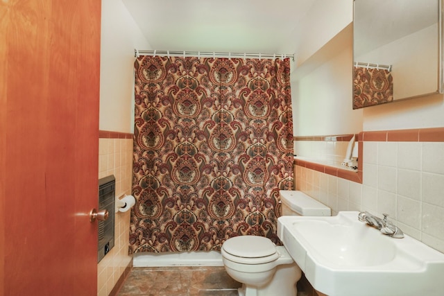 bathroom with toilet, wainscoting, a sink, and tile walls