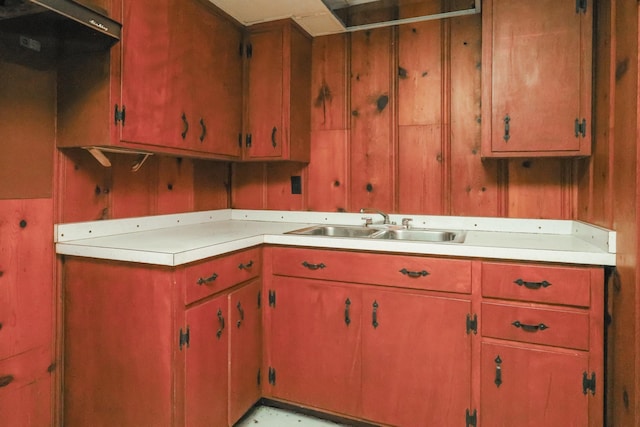 kitchen with light countertops, wood walls, a sink, and under cabinet range hood