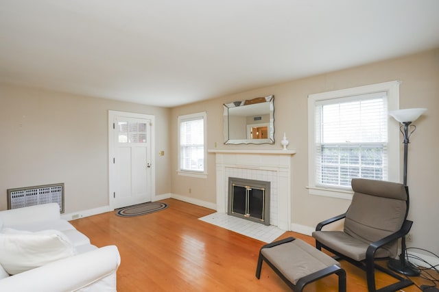 living area with light wood-style floors, a tile fireplace, radiator, and baseboards