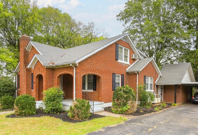 view of front facade featuring a porch, an attached carport, brick siding, a wall mounted AC, and a chimney