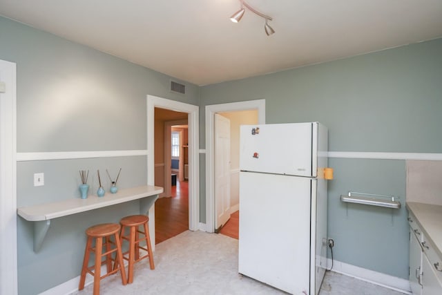 kitchen featuring baseboards, visible vents, a breakfast bar area, and freestanding refrigerator