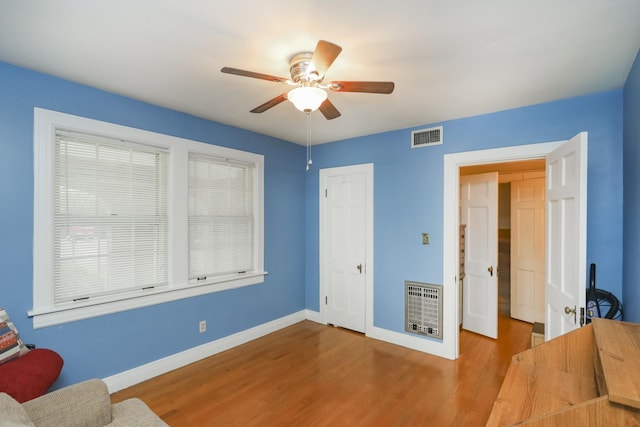 living area with ceiling fan, wood finished floors, visible vents, and baseboards