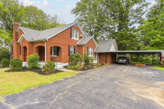 view of front of house with an attached carport, brick siding, driveway, and a chimney