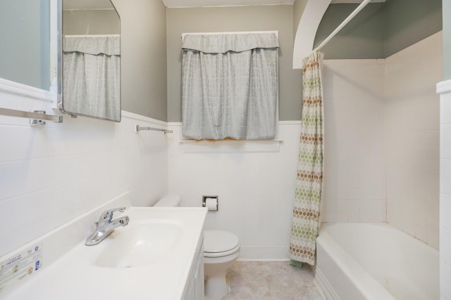 bathroom featuring shower / tub combo, toilet, a wainscoted wall, vanity, and tile walls