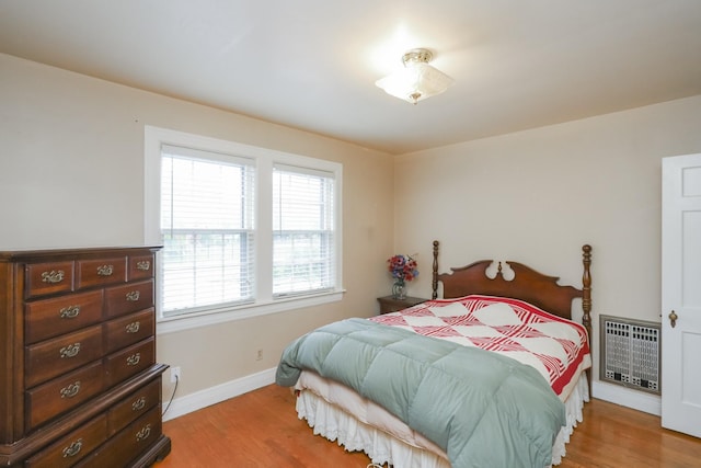 bedroom featuring baseboards, heating unit, and light wood-style floors