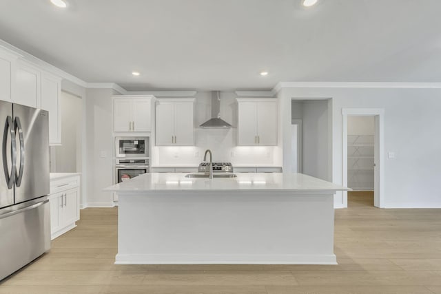 kitchen with light wood finished floors, stainless steel appliances, light countertops, a sink, and wall chimney exhaust hood