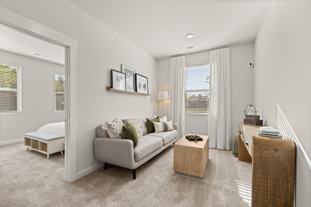 living area featuring a healthy amount of sunlight, light carpet, visible vents, and baseboards