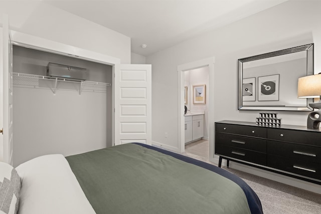 bedroom featuring a closet, light colored carpet, baseboards, and ensuite bathroom