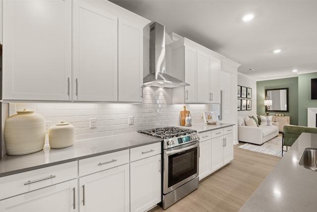 kitchen featuring backsplash, open floor plan, light wood-type flooring, stainless steel gas range oven, and wall chimney exhaust hood