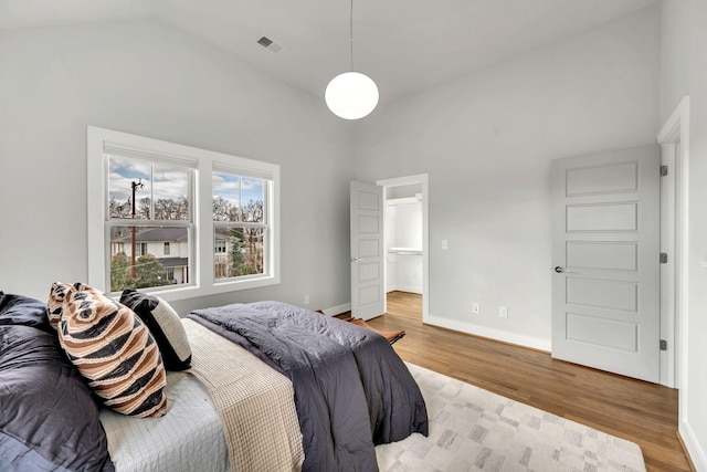 bedroom with high vaulted ceiling, wood finished floors, visible vents, and baseboards