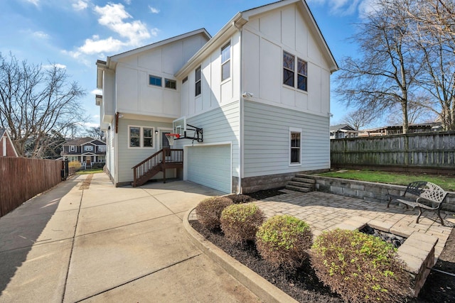 rear view of house with board and batten siding, concrete driveway, fence, and an attached garage