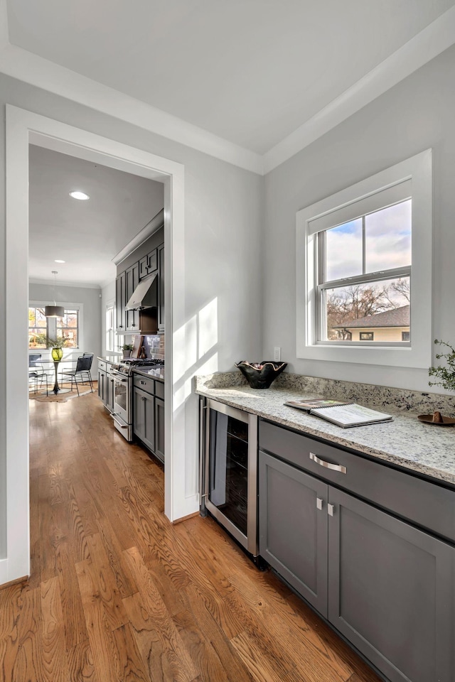 kitchen featuring gray cabinets, stainless steel gas stove, light wood-type flooring, beverage cooler, and under cabinet range hood