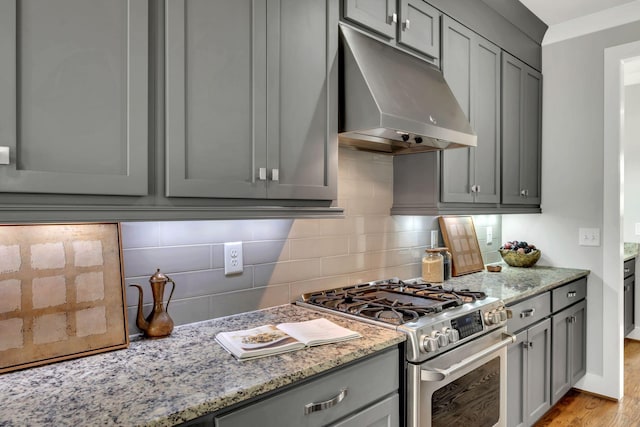 kitchen with stainless steel gas stove, under cabinet range hood, gray cabinets, and decorative backsplash