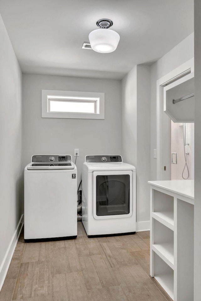 clothes washing area with laundry area, separate washer and dryer, visible vents, baseboards, and light wood-type flooring