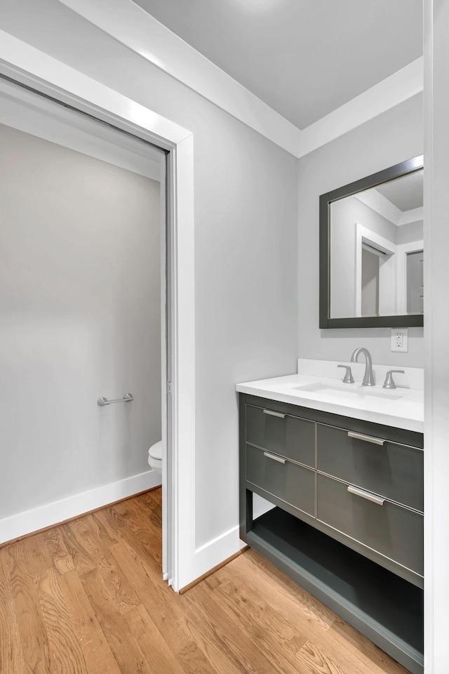 bathroom featuring baseboards, toilet, ornamental molding, wood finished floors, and vanity