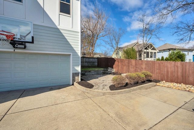 exterior space featuring a garage, concrete driveway, fence, and a patio