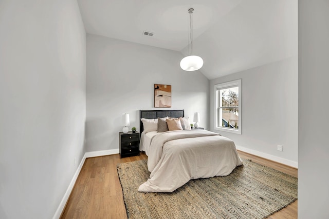 bedroom featuring visible vents, vaulted ceiling, baseboards, and wood finished floors