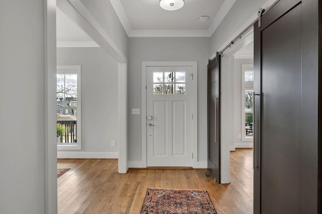 entrance foyer featuring crown molding, a barn door, light wood-style floors, and a healthy amount of sunlight