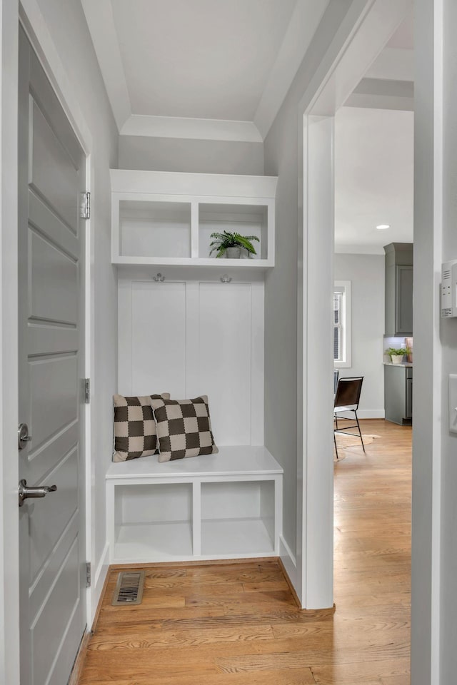 mudroom with light wood-type flooring, baseboards, visible vents, and crown molding