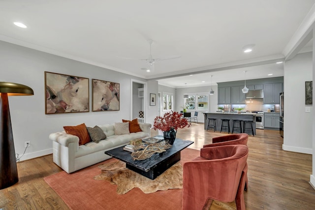 living room featuring ornamental molding, baseboards, light wood finished floors, and a ceiling fan