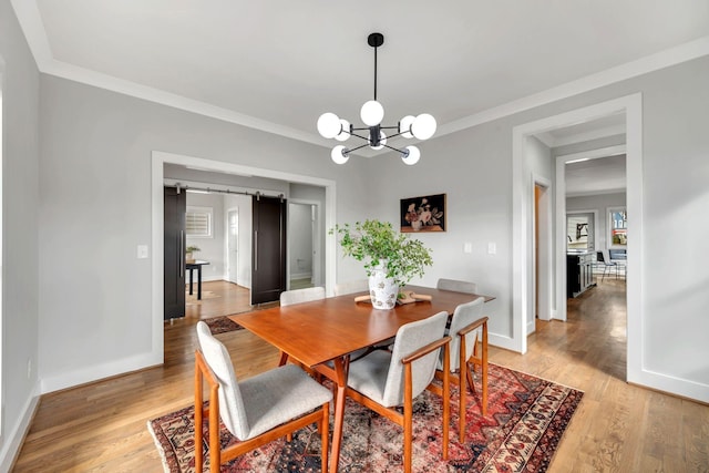 dining area featuring ornamental molding, a barn door, light wood-type flooring, and baseboards