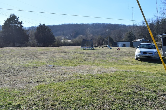 view of yard with a trampoline, a view of trees, and a playground