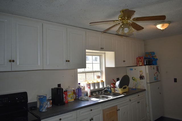 kitchen featuring dark countertops, freestanding refrigerator, white cabinets, a sink, and black / electric stove