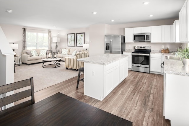 kitchen featuring a center island, light wood finished floors, appliances with stainless steel finishes, open floor plan, and white cabinets