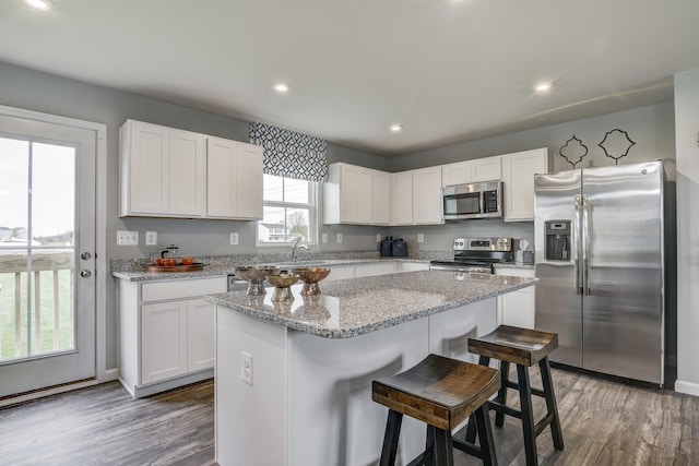 kitchen featuring a breakfast bar, a center island, appliances with stainless steel finishes, white cabinetry, and wood finished floors