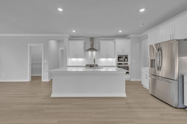 kitchen featuring stainless steel appliances, white cabinets, light wood-style floors, and wall chimney range hood