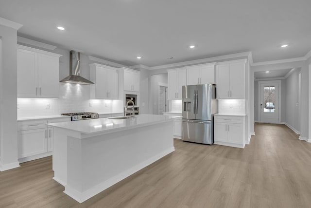 kitchen featuring range, stainless steel fridge with ice dispenser, light wood-style flooring, wall chimney exhaust hood, and a sink