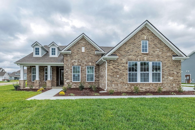 craftsman-style home with a front yard, covered porch, and brick siding