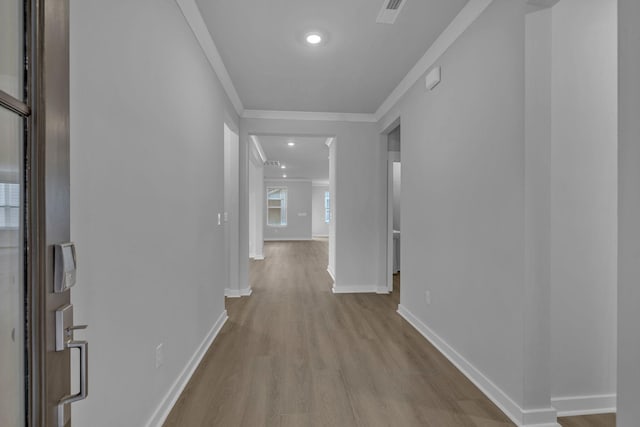 corridor featuring ornamental molding, wood finished floors, visible vents, and baseboards