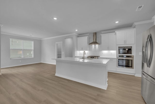 kitchen with visible vents, wall chimney exhaust hood, appliances with stainless steel finishes, a kitchen island with sink, and a sink