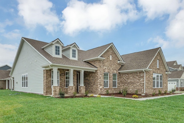 view of front of house with a shingled roof, a front yard, a porch, and brick siding